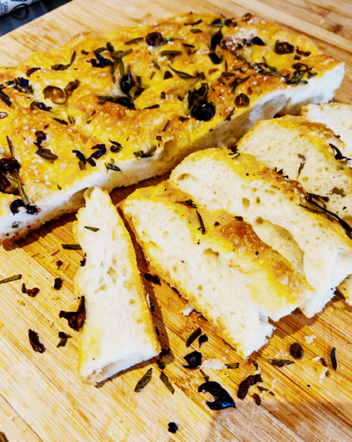 Fresh focaccia sliced on a wooden board with herbs